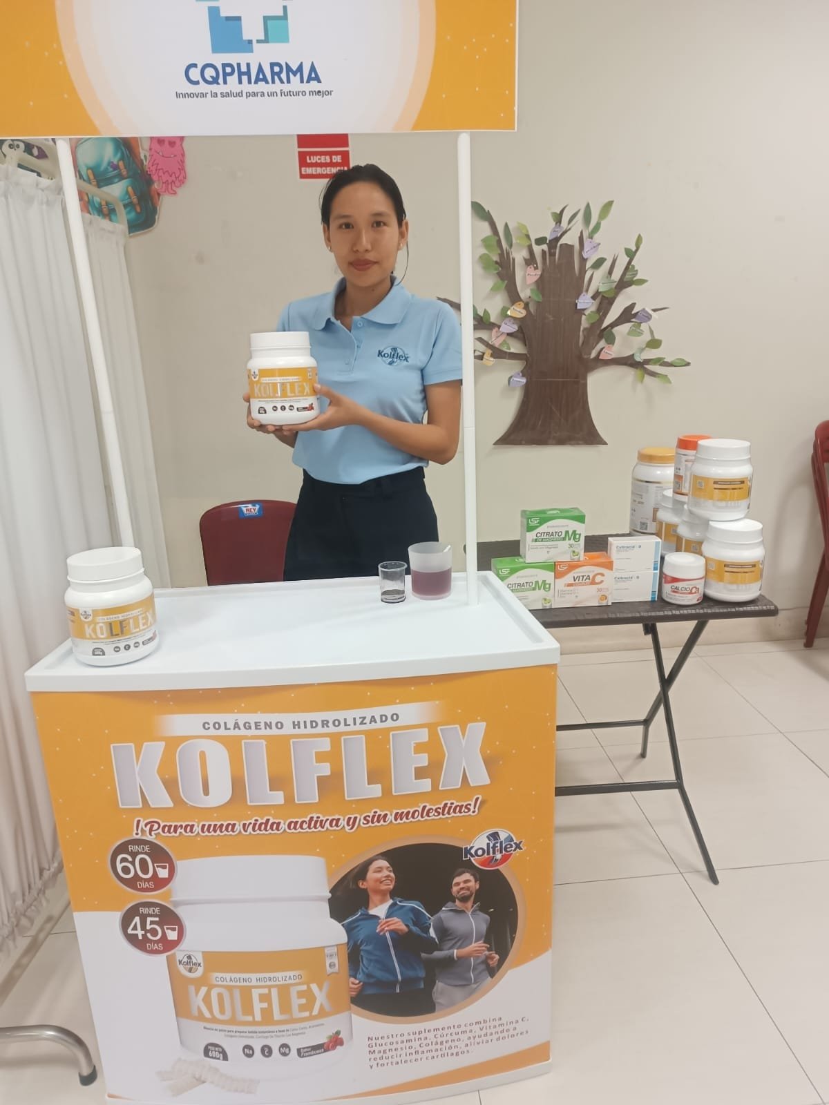 Asesora de CQPharma sostiene un frasco de Kolflex detrás de un mostrador con la línea de productos.